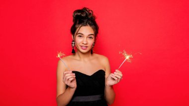 Havai fişekler ve insan konsepti - gülümseyen genç kadın ya da genç kız maytaplı mutlu kadın kırmızı arka planda siyah elbiseyle kutluyor. Kız kameraya gülümsüyor.