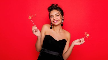 Havai fişekler ve insan konsepti - gülümseyen genç kadın ya da genç kız maytaplı mutlu kadın kırmızı arka planda siyah elbiseyle kutluyor. Kız kameraya gülümsüyor.