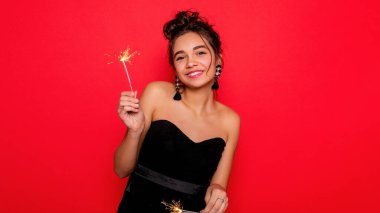 Havai fişekler ve insan konsepti - gülümseyen genç kadın ya da genç kız maytaplı mutlu kadın kırmızı arka planda siyah elbiseyle kutluyor. Kız kameraya gülümsüyor. dans etmek