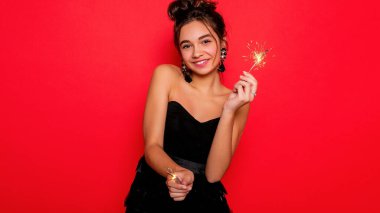 Havai fişekler ve insan konsepti - gülümseyen genç kadın ya da genç kız maytaplı mutlu kadın kırmızı arka planda siyah elbiseyle kutluyor. Kız kameraya gülümsüyor, dans ediyor.