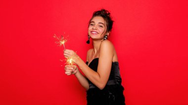 Havai fişekler ve insan konsepti - gülümseyen genç kadın ya da genç kız maytaplı mutlu kadın kırmızı arka planda siyah elbiseyle kutluyor. Kız kameraya gülümsüyor.