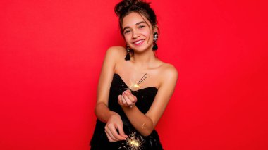 Havai fişekler ve insan konsepti - gülümseyen genç kadın ya da genç kız maytaplı mutlu kadın kırmızı arka planda siyah elbiseyle kutluyor. Kız kameraya gülümsüyor.