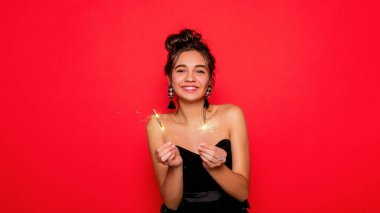 Havai fişekler ve insan konsepti - gülümseyen genç kadın ya da genç kız maytaplı mutlu kadın kırmızı arka planda siyah elbiseyle kutluyor. Kız kameraya gülümsüyor.