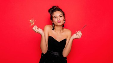 Havai fişekler ve insan konsepti - gülümseyen genç kadın ya da genç kız maytaplı mutlu kadın kırmızı arka planda siyah elbiseyle kutluyor. Kız kameraya gülümsüyor, dudaklar pipetle