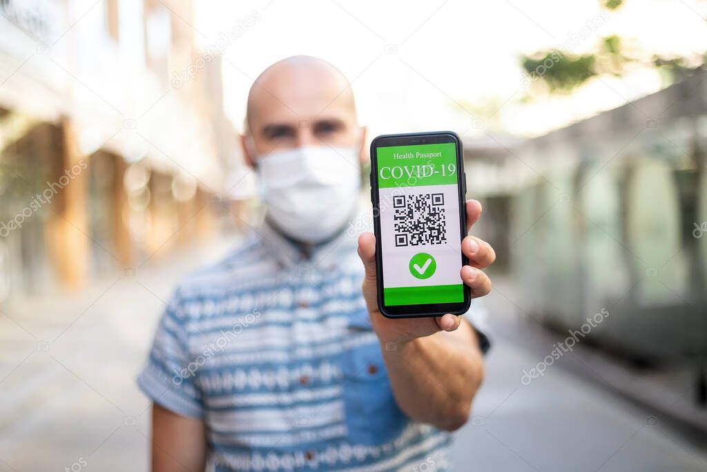 Covid-19 Protection Concept. Happy young man holding mobile phone with digital international health passport application, confirming vaccination, ready for travel