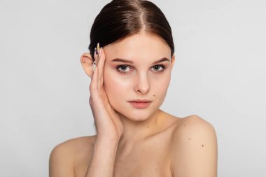 Temiz, taze tenli ve koyu renkli genç bir kadın sağ eliyle kendi yüzüne dokunuyor. Kozmetik, güzellik ve kaplıca. Yüz bakımı.