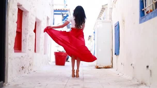 快乐的女人穿着红色的长裙 头发上插着一朵红花 她正在参观著名的旅游胜地 美丽时髦的黑发女人跳舞离去 裙子在风中飘扬 — 图库视频影像