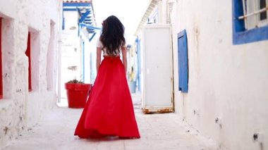 Happy woman in red long skirt and with a red flower in her hair. She is visiting famous tourist attraction. Beautiful fashionable brunette woman backs away and skirt flutters in the wind
