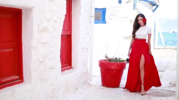 快乐的女人穿着红色的长裙 头发上插着一朵红花 她正在参观著名的旅游胜地 穿着红色夏装的漂亮女孩走在街上 — 图库视频影像