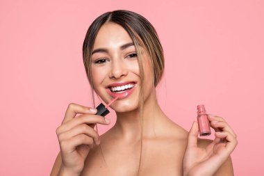 Sexy woman lips with pink makeup and gloss, closeup of a young dark-skinned woman applying lipgloss with brush on a white background