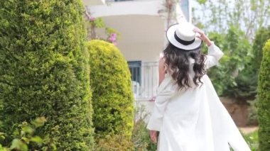 Eski Avrupa şehrinin caddesinde yürüyen şapkalı ve elbiseli kadın. Güneşli bir günde beyaz duvarlar arasında dar sokağa çıkan bir kız.