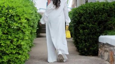 Beyaz şapkalı, beyaz elbiseli, beyaz şapkalı, yeşil çalılıklı genç bir kadın oteli gözetliyor..