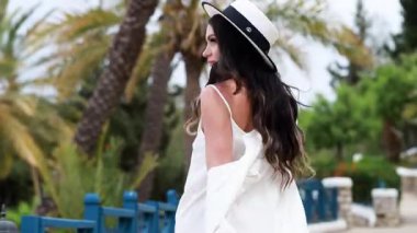 Beyaz şapkalı, beyaz elbiseli genç bir kadın. Beyaz duvarları ve güzel yeşil çalıları olan şehirde dolaşıyor. Güzel bir ara sokak..