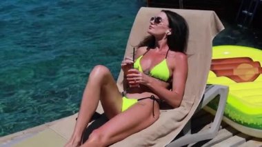 Lüks bir otelde rahat rahat uzanan zarif bir bayan. Kadın kolları havada, özgürlük ve lüks tatil konsepti, bir kokteyl ve kablosuz kulaklıkla müzik dinlemek
