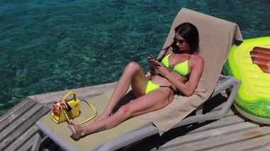 Turkuaz denizde cep telefonu kullanan turkuaz şamandırada açık yeşil mayo giyen tatilci kadın. Rahatlayan kız bikinili tatil köyünde tatilin tadını çıkarıyor..