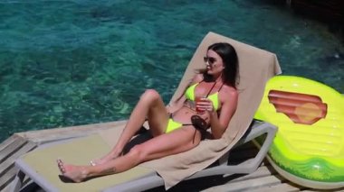 Lüks bir otelde rahat rahat uzanan zarif bir bayan. Kadın kolları havada, özgürlük ve lüks tatil konsepti, bir kokteyl ve kablosuz kulaklıkla müzik dinlemek