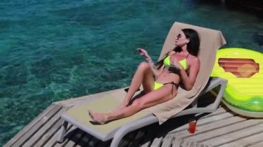 Lüks bir otelde rahat rahat uzanan zarif bir bayan. Kadın kolları havada, özgürlük ve lüks tatil konsepti, bir kokteyl ve kablosuz kulaklıkla müzik dinlemek