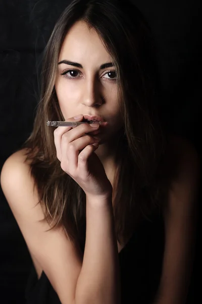 Элегантная брюнетка курит сигарету на черном фоне — стоковое фото