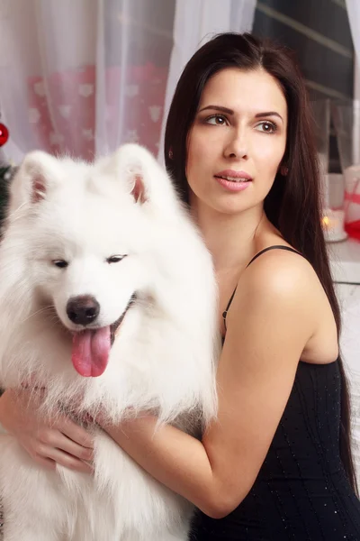 Bela morena jovem mulher vestido preto longo com um cão branco-neve Samoyed estúdio husky em tons de velas marrons — Fotografia de Stock