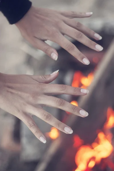 Meisje opwarming van de aarde zijn handen op kampvuur in bos — Stockfoto