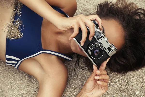 beautiful girl with camera in a swimsuit on the sand