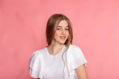 Yumuşak gülümseyen stüdyo resmi, pembe arka planda beyaz fırfırlı bluz, minimal modern estetik.