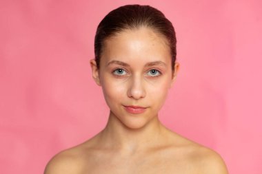 Hafif açılı pembe arkaplan portresi, doğal güzellik ve pürüzsüz cilt odağı.