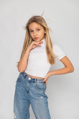 Beyaz tişörtlü ve beyaz arka planda mavi kotlu genç bir kızın tüm vücut portresi..