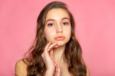 Soft headshot with hand near chin, calm editorial look on pink background.
