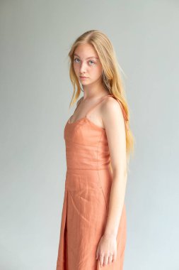 Full-body studio portrait of blonde woman in peach dress on gray background, minimal fashion lookbook.
