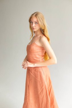 Mercan elbisesiyle yan yana pozlar, tarafsız arkaplan üzerine temiz editoryal moda.