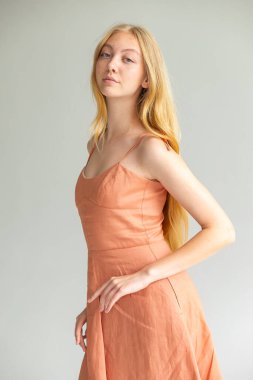 Sakin ifadeli moda portresi, mercan elbisesi, temiz minimum arkaplan.
