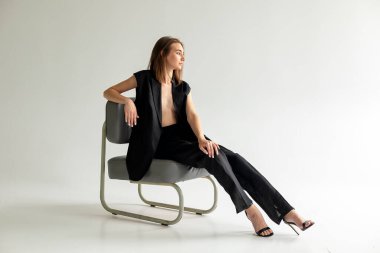 Tasarımcı koltuğunda rahat bir şekilde oturan kadın, temiz stüdyo modası ve iş stili konsepti.