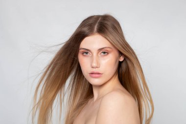 Saç hareketi, doğal ten ve gri üzerine editoryal aydınlatma ile yakın güzellik portresi.