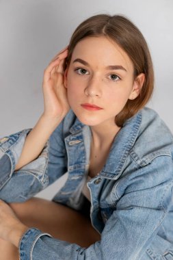 Headshot in denim jacket, soft gaze and minimal studio lighting.
