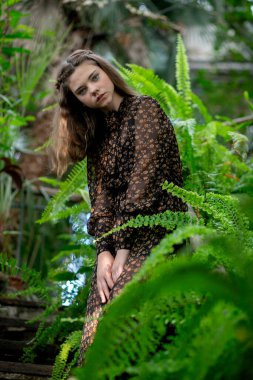 Rüya gibi orman portresi, eğrelti otlarıyla çevrili desenli elbiseli kadın, doğal uyum konsepti..