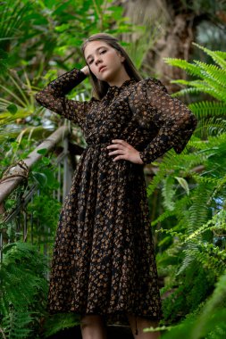 Vertical portrait, woman in patterned dress among tropical plants, slow living concept.