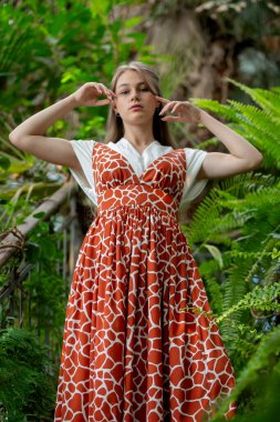Kendine güvenen pozlar, elleri başının üstünde, kırmızı desenli elbiseler, yemyeşil bitkiler ve sinematik ruh hali..