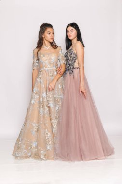 Duo portrait in formal gowns, minimal studio backdrop, wedding party or prom fashion marketing.