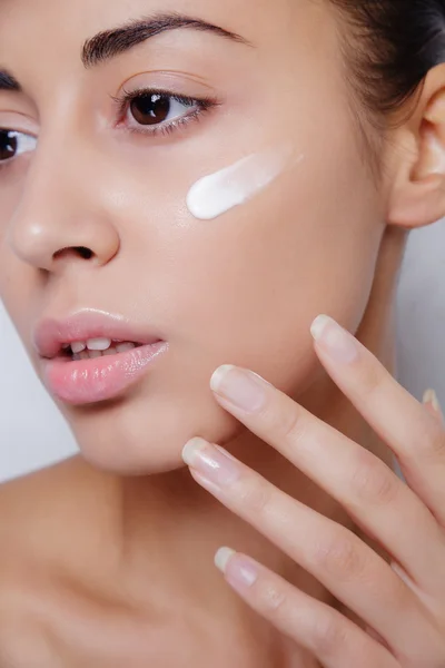 Modelo bonito aplicando tratamento de creme cosmético em seu rosto branco — Fotografia de Stock