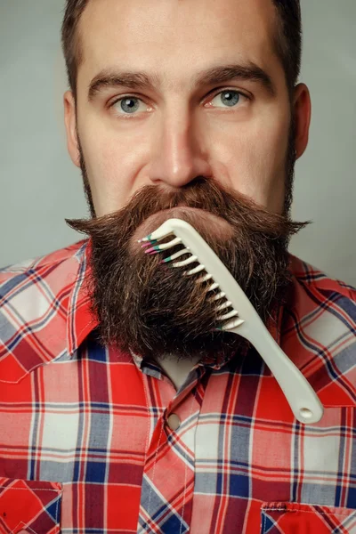Giovane uomo pettinare la barba e baffi su sfondo grigio — Foto Stock