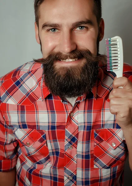 young man comb his beard and moustache on gray background