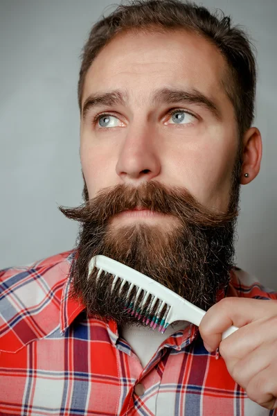 young man comb his beard and moustache on gray background