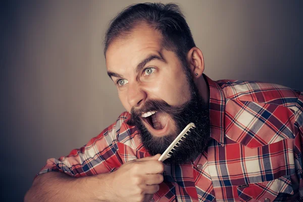 Giovane uomo pettinare la barba e baffi su sfondo grigio — Foto Stock