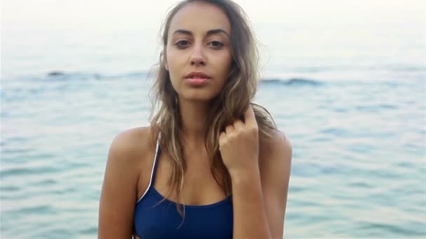 Retrato de moda ao ar livre de mulher sexy morena atlética posando com vista para o mar, lentamente. em um maiô azul, dia ensolarado . — Vídeo de Stock