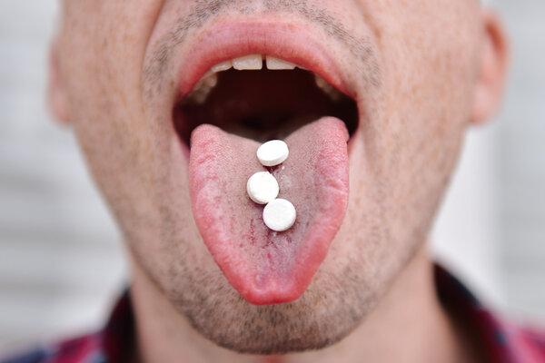 Вырезанный кадр человека с таблеткой в языке
