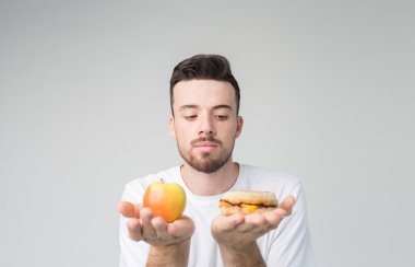 Bearded man in a white shirt on a light background holding a hamburger and an apple clipart