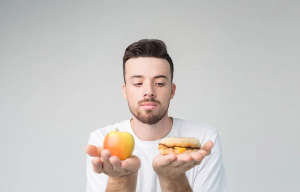 Skäggig man i en vit skjorta på en bakgrund håller en hamburgare och ett äpple — Stockfoto