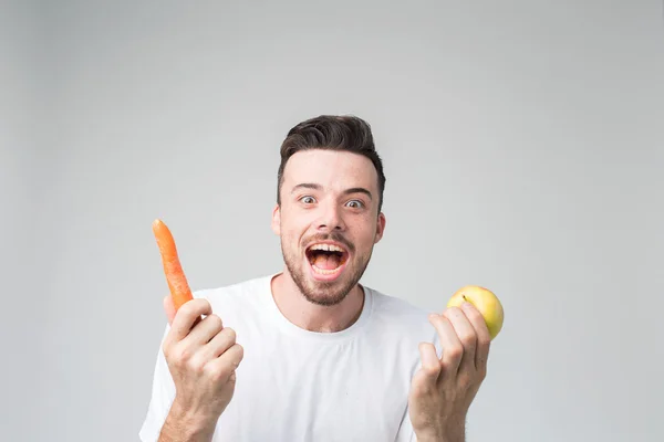 Чоловік у білій сорочці ізольований на світлому фоні, що тримає моркву та яблуко . — стокове фото