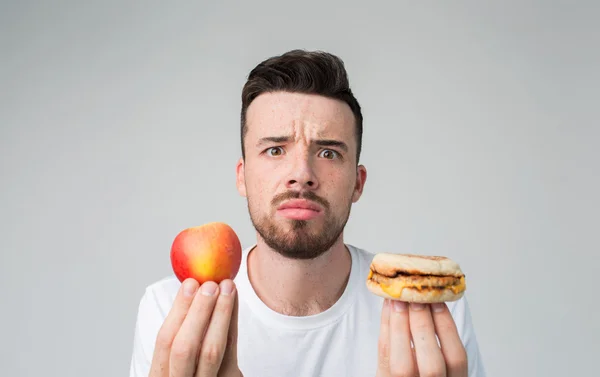 햄버거와 사과 들고 밝은 배경에 흰 셔츠에 수염된 남자 — 스톡 사진